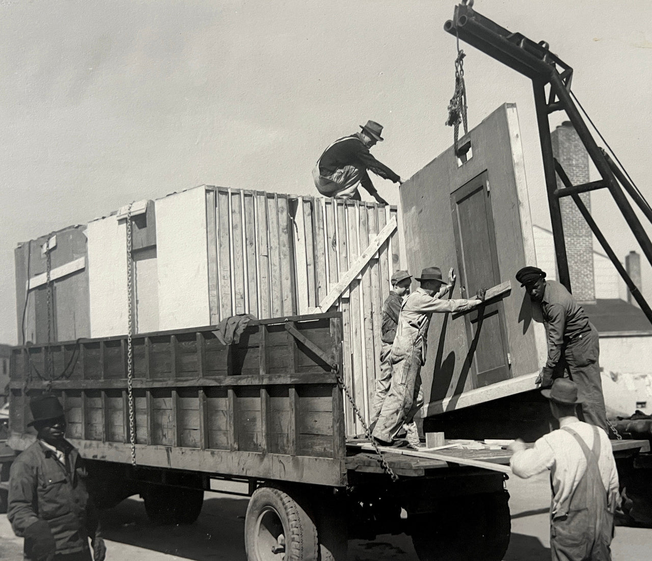 Historical black and white photo of men loading sections of temporary war housing onto a truck in Portsmouth, VA.