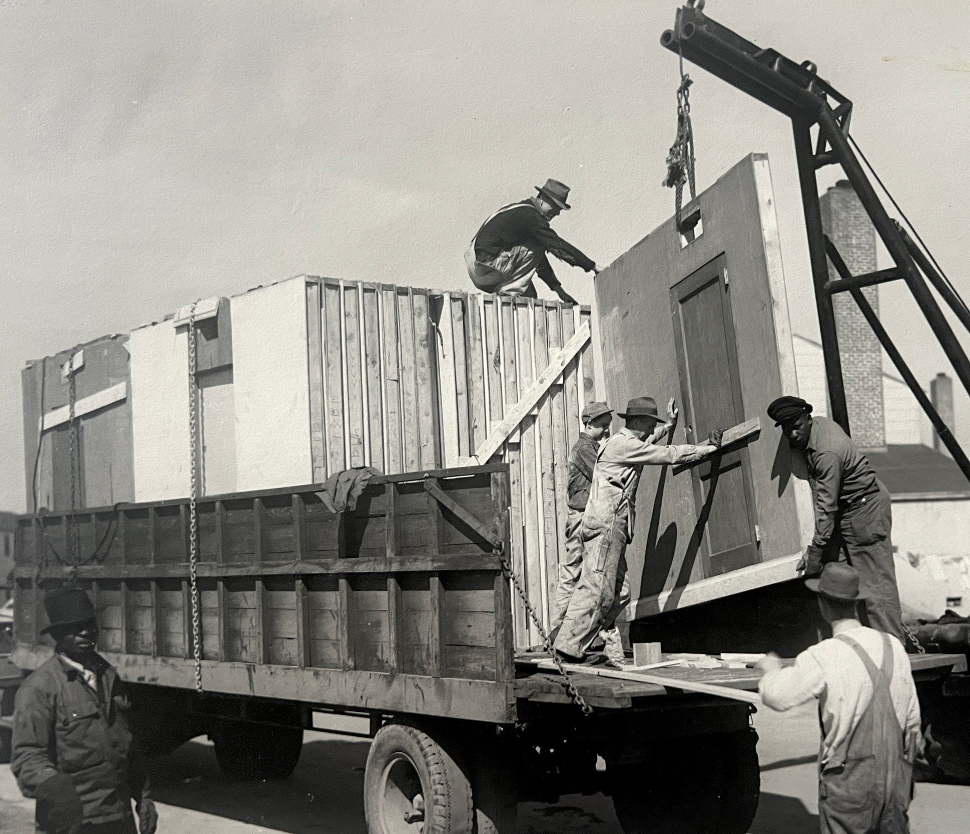Historical black and white photo of men loading sections of temporary war housing onto a truck in Portsmouth, VA.